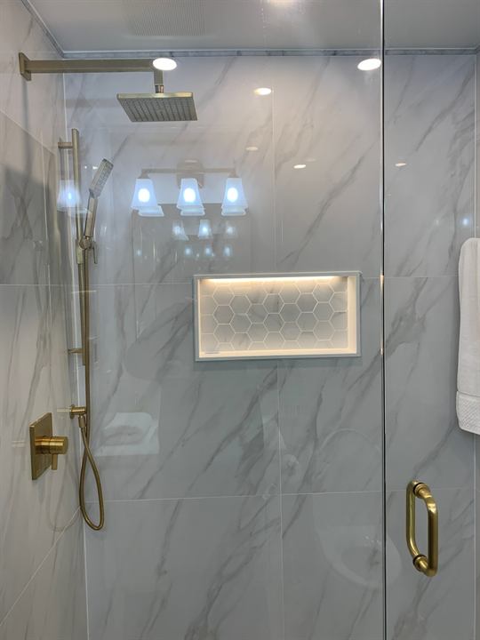Shower with brushed gold fixtures, lit niche and linear drain
