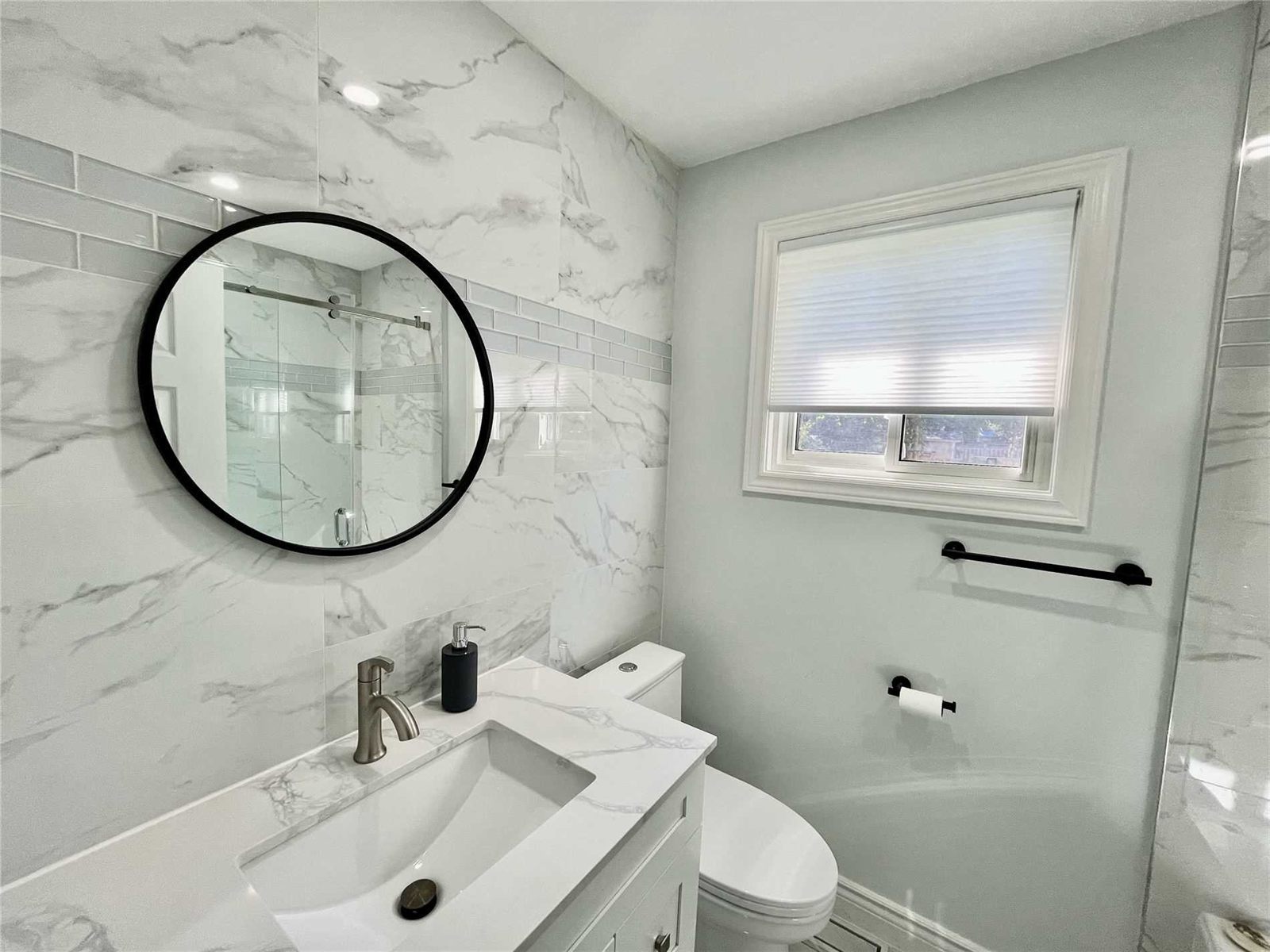 Full bathroom renovation with marble-look tile and round mirror