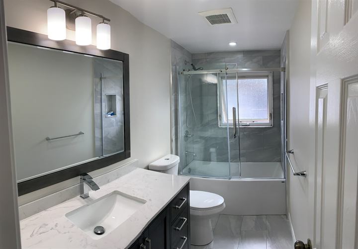 Full bathroom renovation with vanity, tub with sliding glass door and porcelain tile